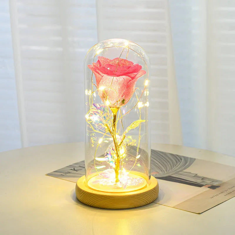 Glass dome containing red eternal roses illuminated by a warm white bendable LED light string.