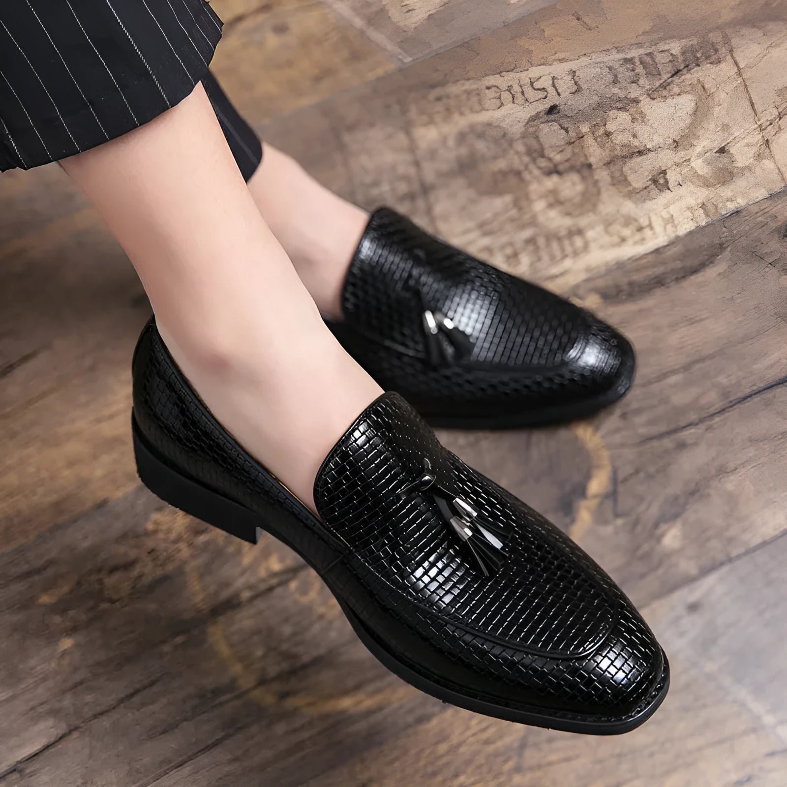 Men's black slip-on leather loafers with a pointed toe and tassel detail on a white background.