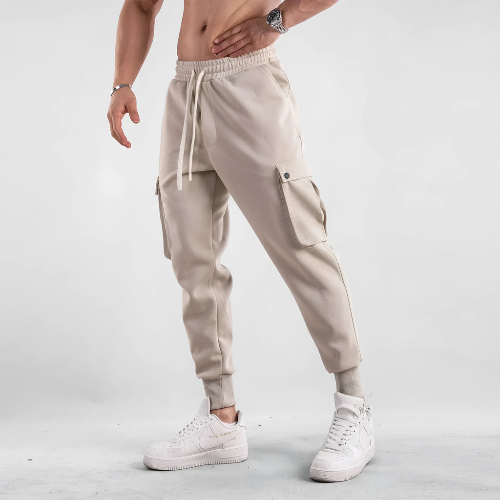 Men's loose beige cotton trousers with an ankle tie and multiple pockets on a casual model.