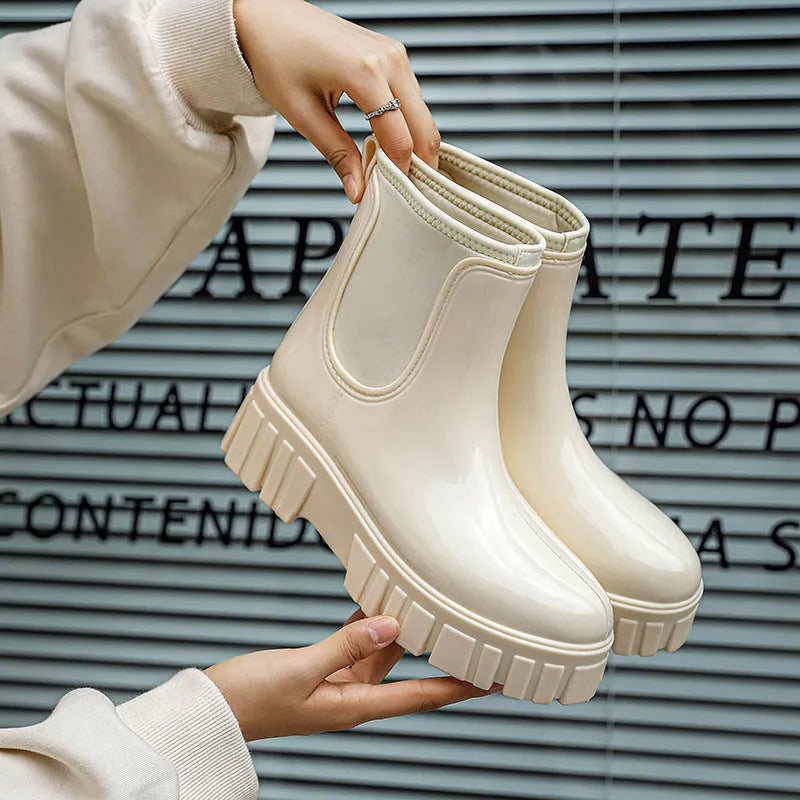 Women's creamy-white PVC rain boots with low tube shaft and flat heel on wet surface