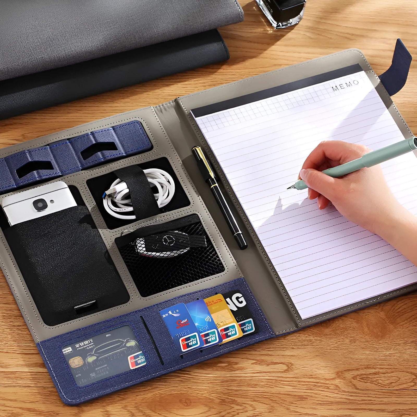 Black leather A4 business folder with optional pen and notepad on a desk.