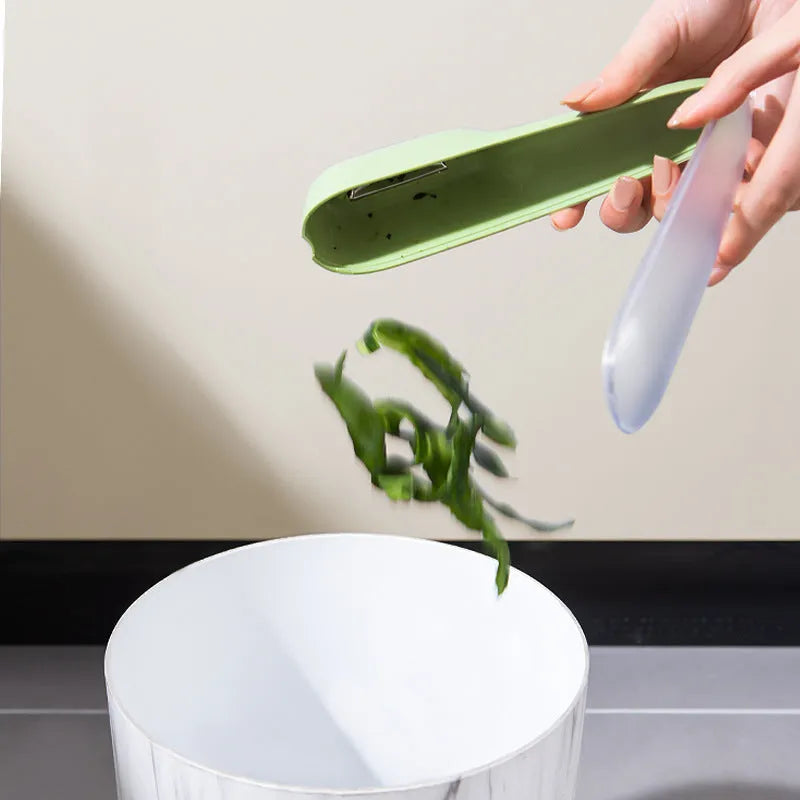 Green vegetable peeler with a storage tube, stainless steel blade, and plastic handle on a kitchen worktop.