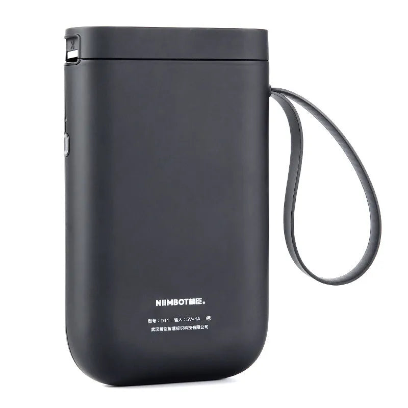 Compact black D11 Bluetooth thermal label printer on a desk next to a smartphone showing the label design app.