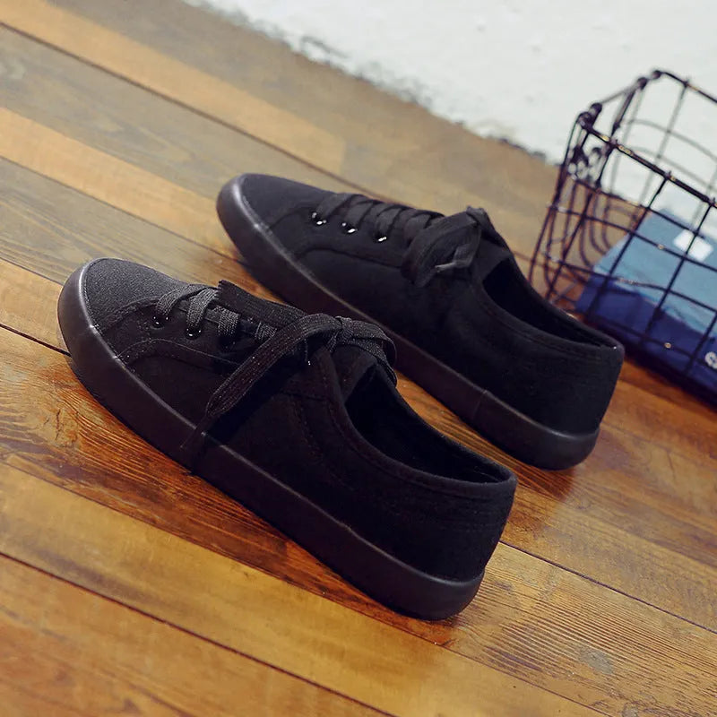 All black canvas low-top lace-up flat shoes for women on a white background