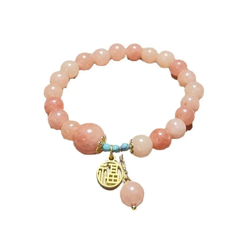 Close-up of a women's pink natural stone and alloy charm bracelet on a wrist, showing adjustable fastening.