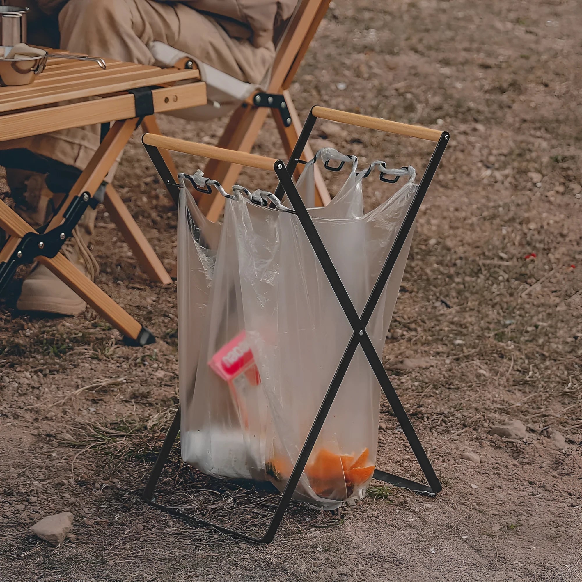 Black iron folding bin rack with wooden handles holding two rubbish bags in an outdoor setting.