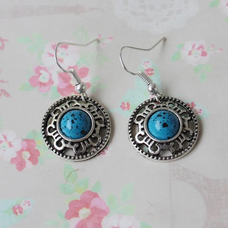 Handmade Miao silver retro earrings with turquoise flower disk and ethnic patterns in black.
