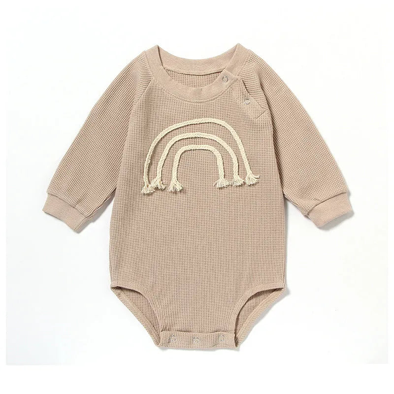 Neutral baby romper in waffle cotton fabric with long sleeves, shown in beige with cotton rope detail.