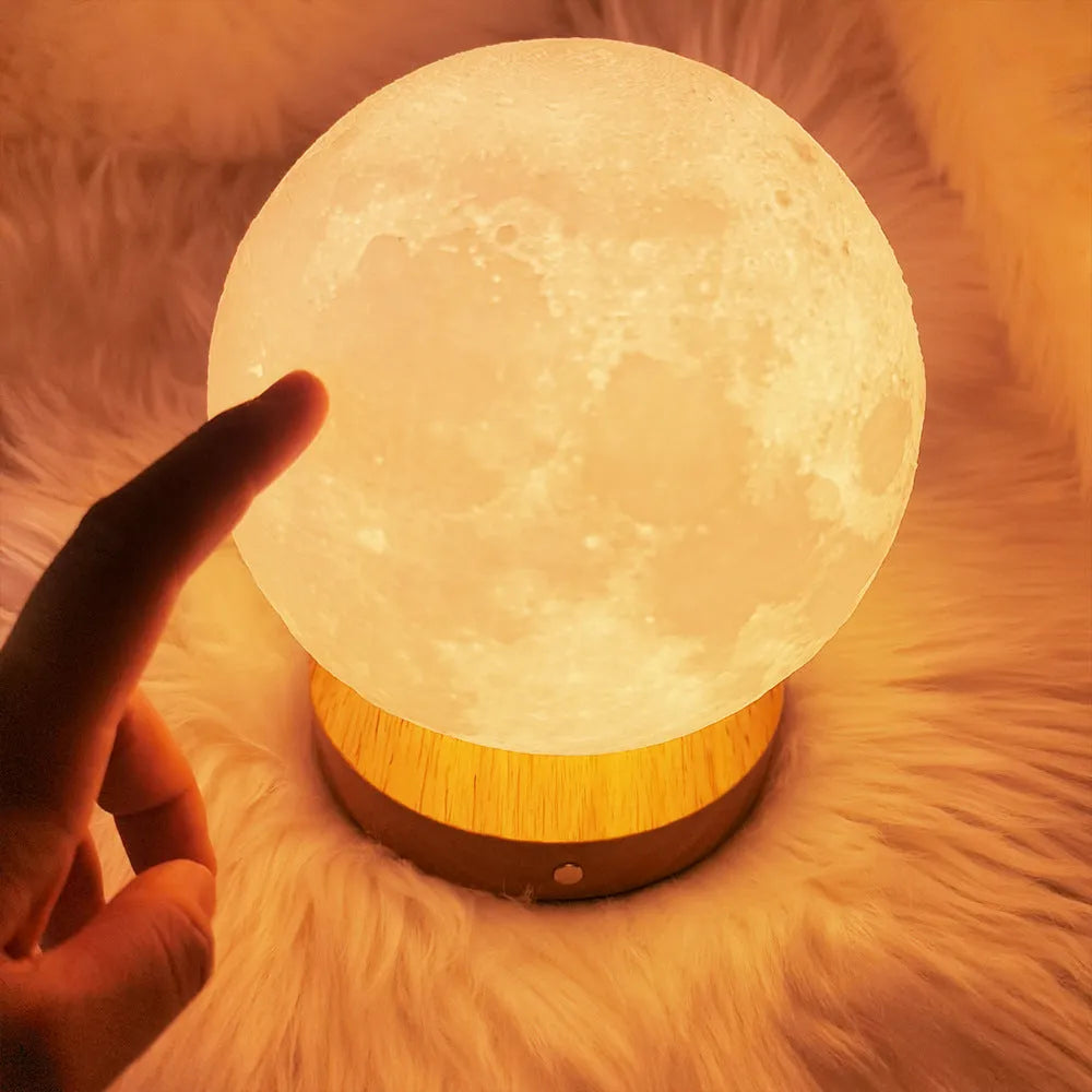 Rotating moon night lamp with wooden base on a table, showing three colour settings and remote control.