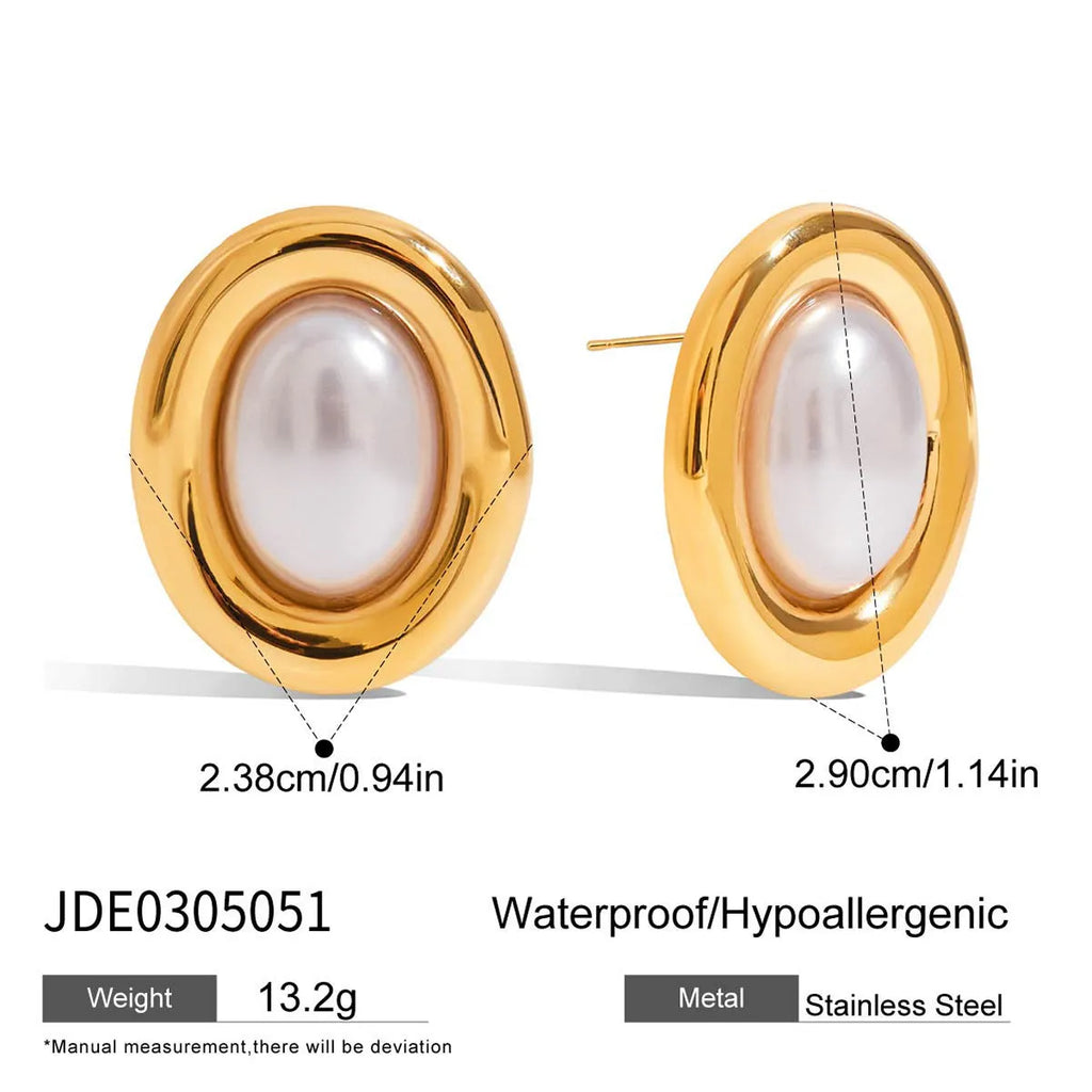 Close-up of a pair of round stainless steel stud earrings with a vintage-style pearl detail on a neutral background.