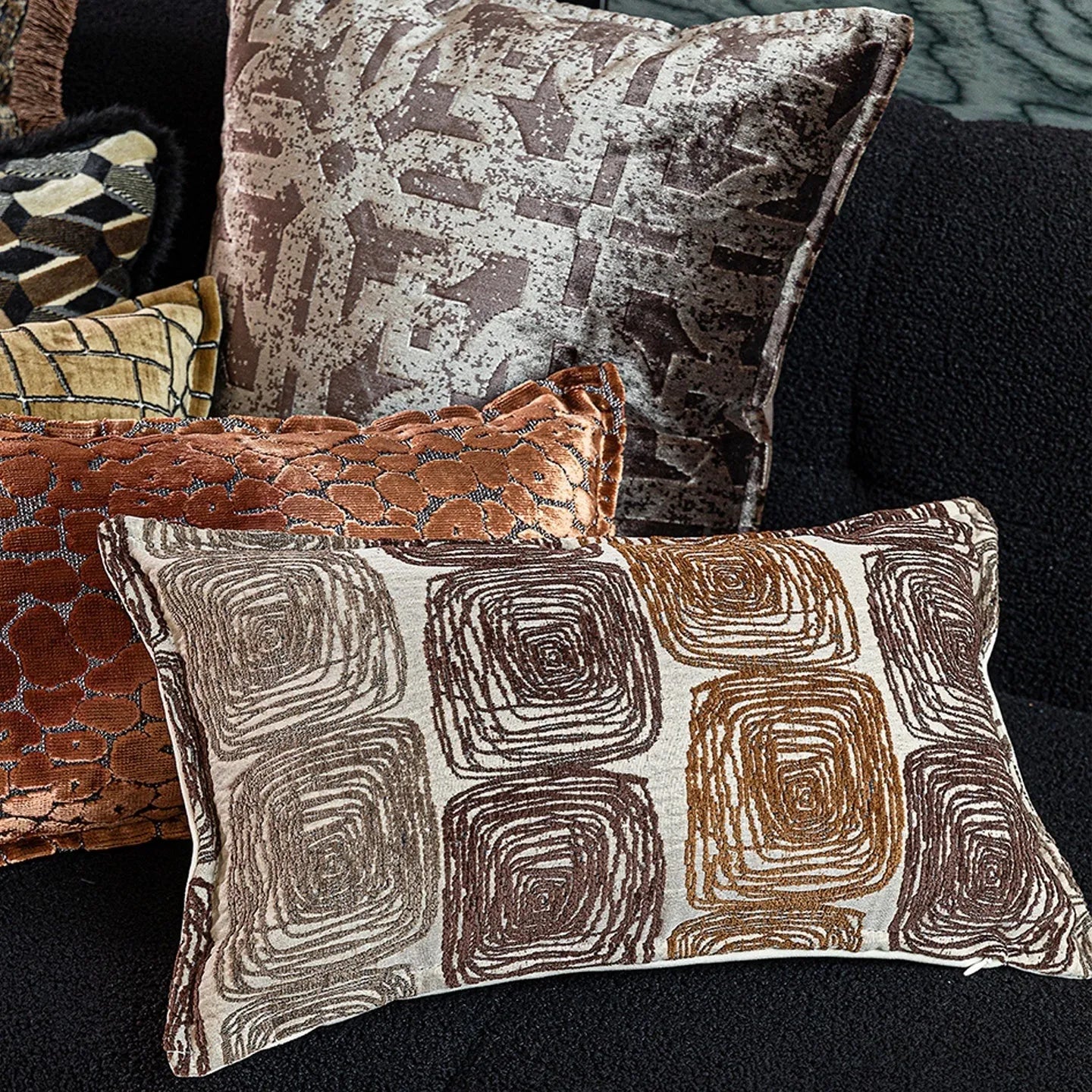 Cream and coffee coloured abstract coil pattern square pillow cover on a grey sofa.