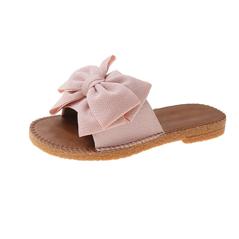Women's beige slip-on sandals with a suede cloth upper, soft rubber sole, and decorative bow.