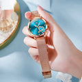 Rose gold tone women's fashion watch with mesh strap, showing options for black, blue, green, pink, red, and white dials.