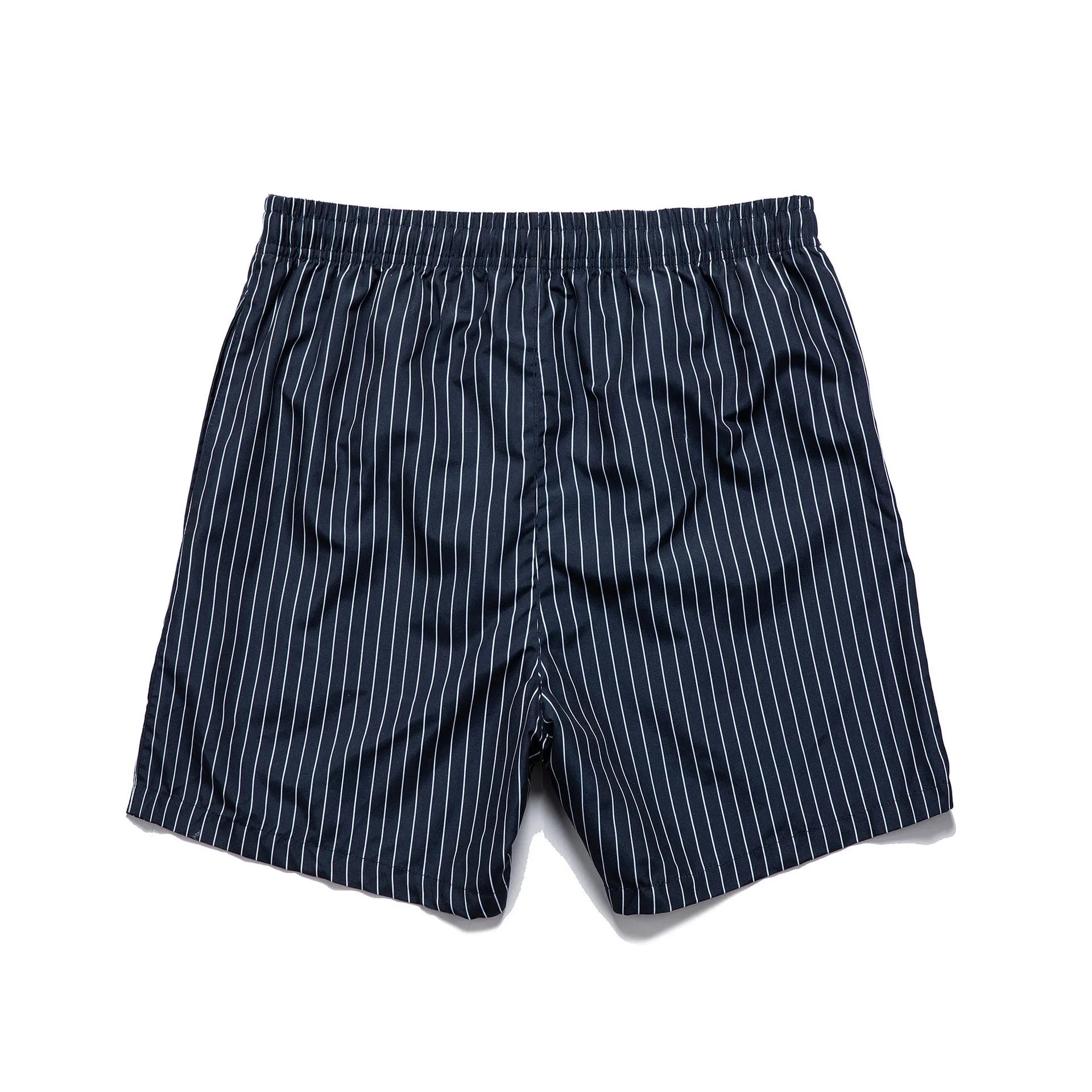 Man wearing navy blue and white striped straight-leg polyester beach shorts on shore.