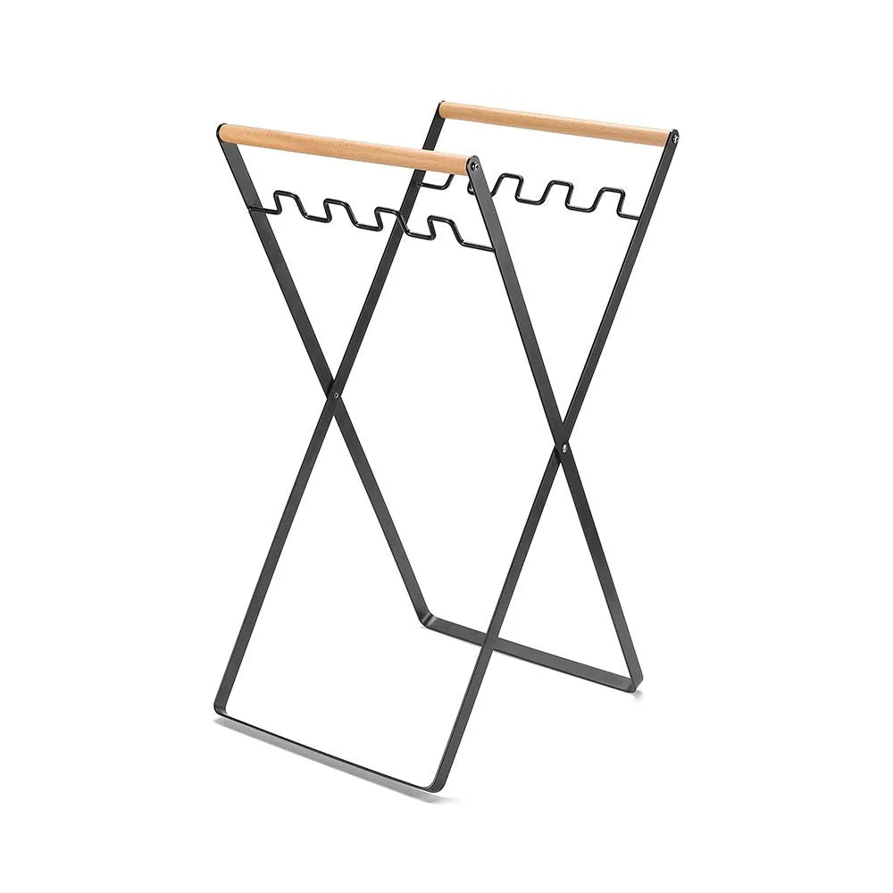 Black iron folding bin rack with wooden handles holding two rubbish bags in an outdoor setting.