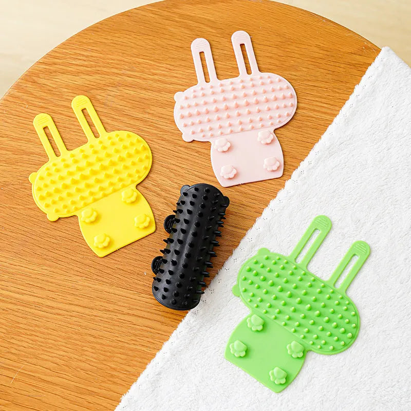Black silicone cat grooming comb with rounded teeth and adjustable mounting strap for table legs.