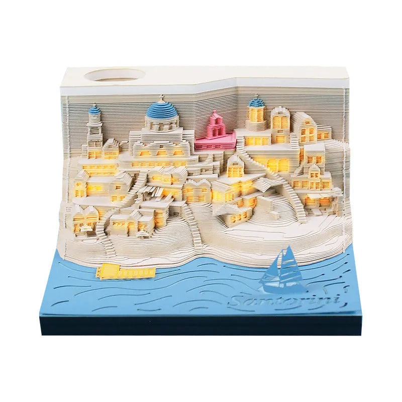 Assembled Santorini beach 3D paper model notepad with decorative lighting on a desk.