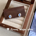 Women's sterling silver oval earrings with heart-wrapped design and blue diamond accents on silver background