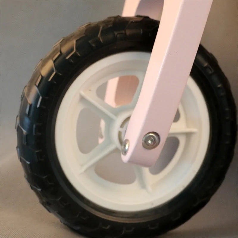 Pink wooden balance scooter for toddlers, 10 inches in size, on a flat surface.