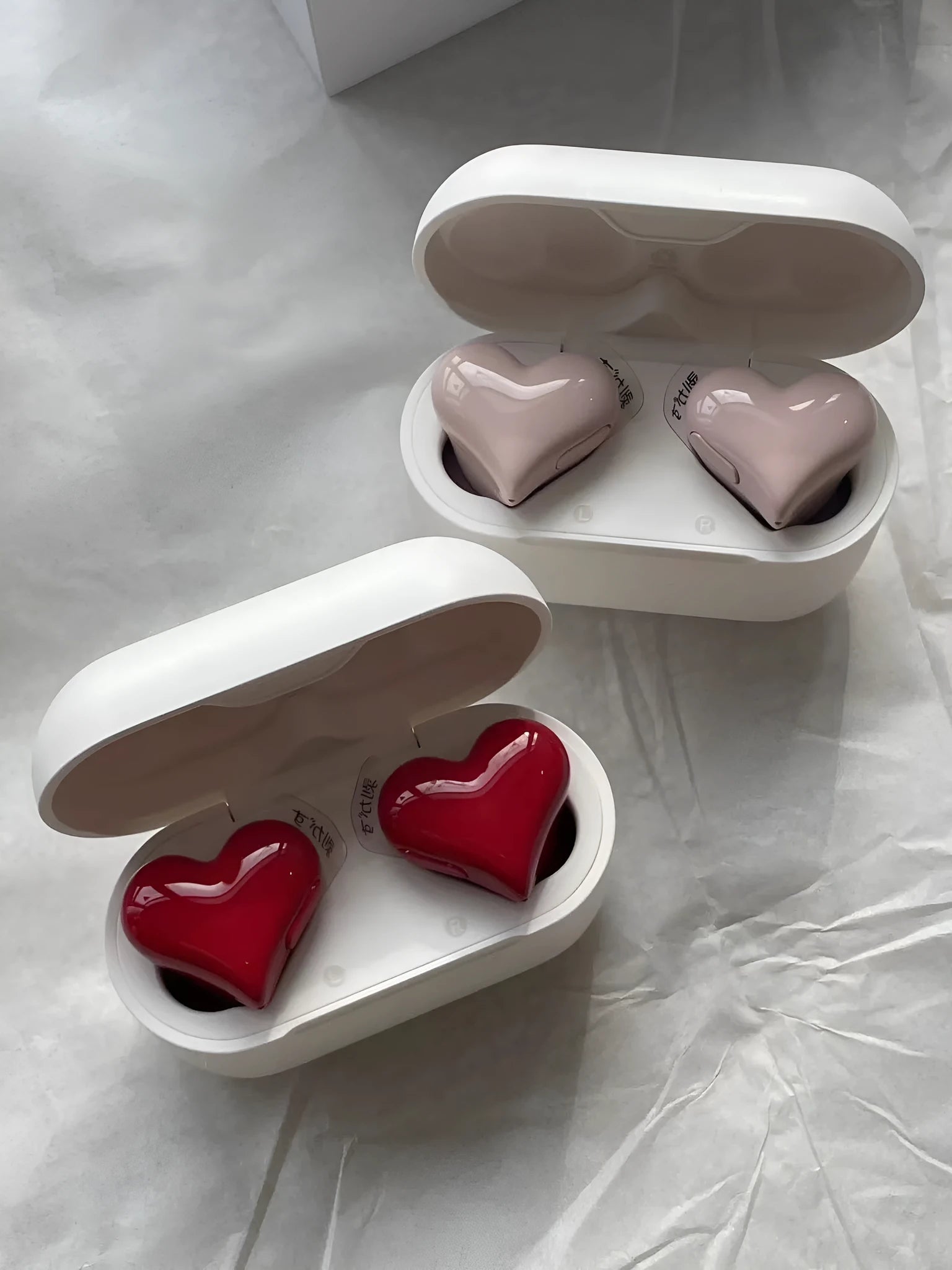 Red and pink heart-shaped wireless Bluetooth in-ear headphones with charging cable.
