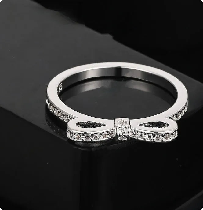 Silver coloured bow-shaped ring with rhinestone and zircon crystal details on a model finger.