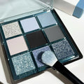 MUGELEEN nine-colour eye shadow palette open showing blue smoked and earth tone shades with matte and shimmer finishes.