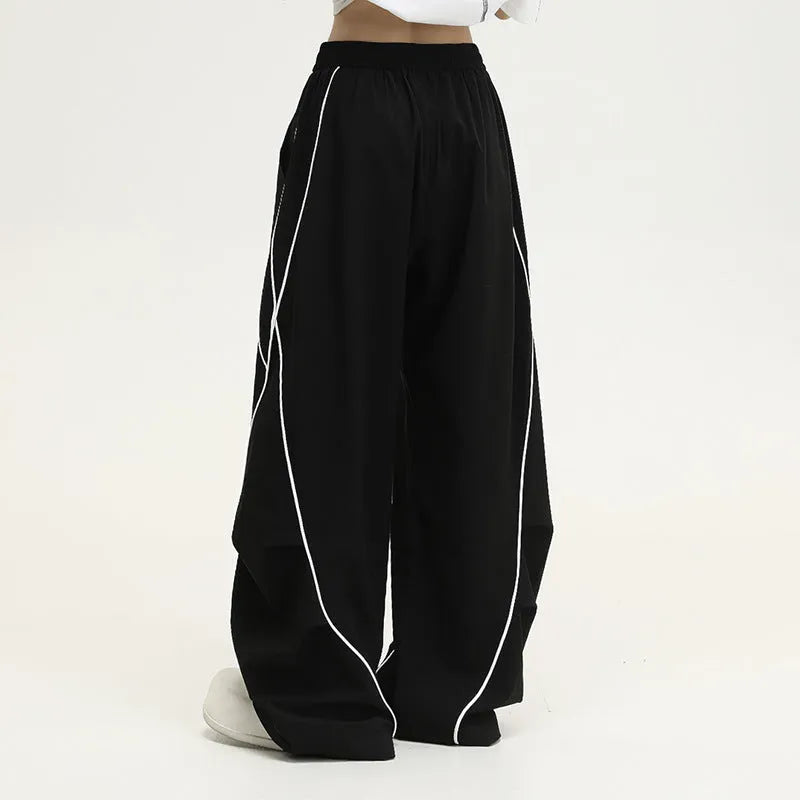 Black trousers with vertical stripes and pleated detail on the legs, showing a loose wide-leg fit.