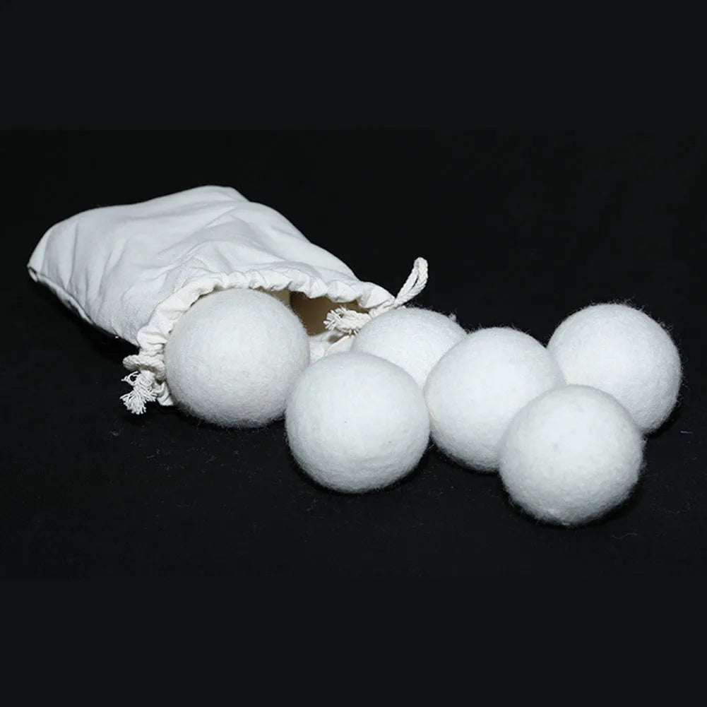 Assorted sized wool drying balls next to a beige cotton drawstring storage bag on a wooden surface.
