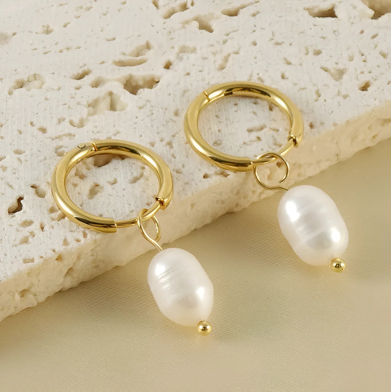 Geometric gold-coloured stainless steel earrings with a white pearl detail on a white background.