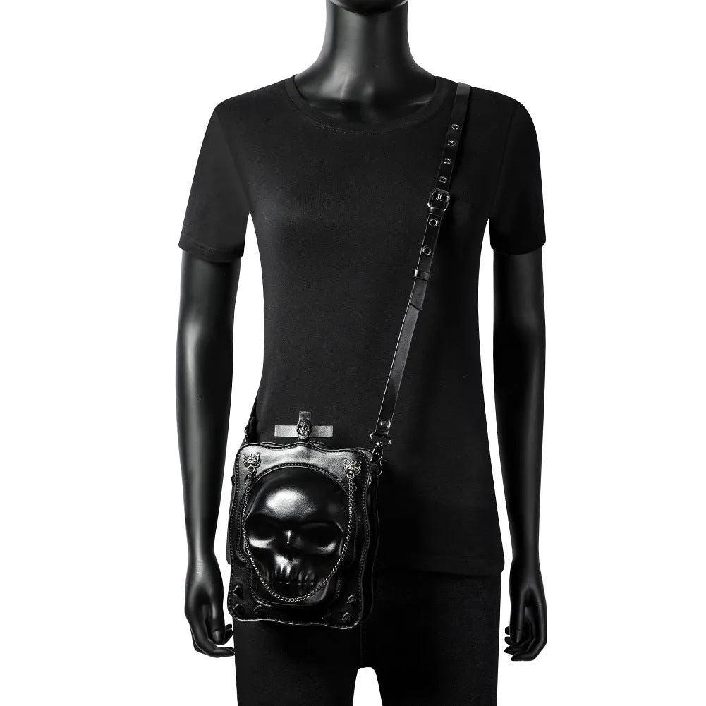Black square mini crossbody bag with embroidered skull design, metal rivets, and a chain shoulder strap.