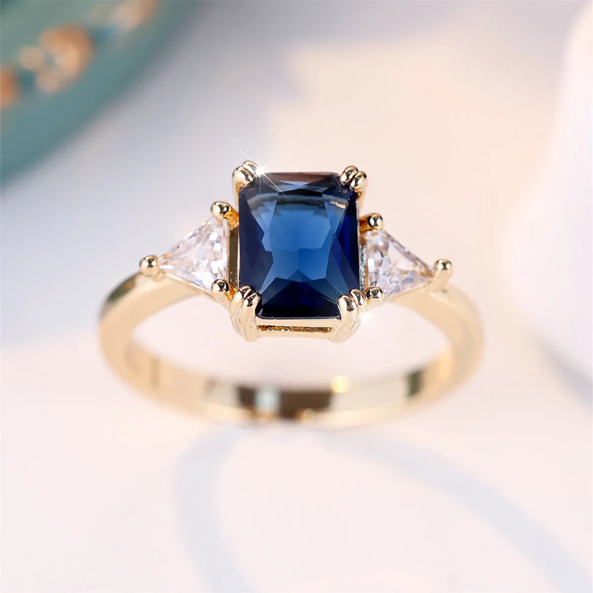 Gold sapphire blue rectangular copper ring for women on a plain background