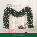 Pink artificial Christmas rattan vine decoration with small fruit clusters and warm white LED lights, coiled on a table.