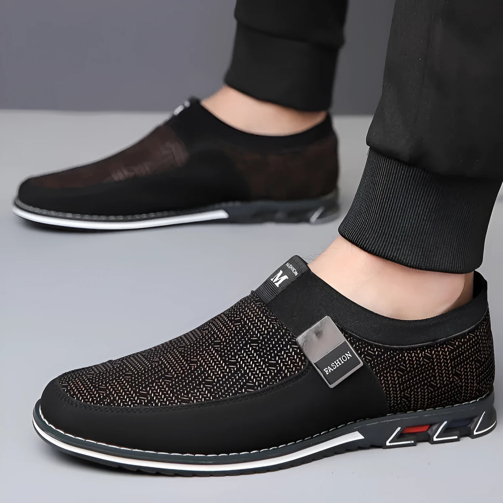 Men's synthetic leather slip-on casual shoe in black, showing square toe and flat rubber sole.