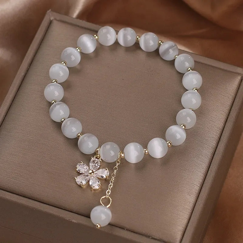 White cat's eye stone women's bracelet with flower and tassel charms on a morganite safety buckle.