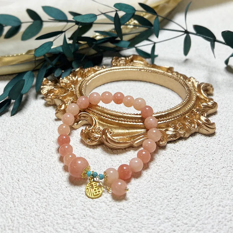 Close-up of a women's pink natural stone and alloy charm bracelet on a wrist, showing adjustable fastening.