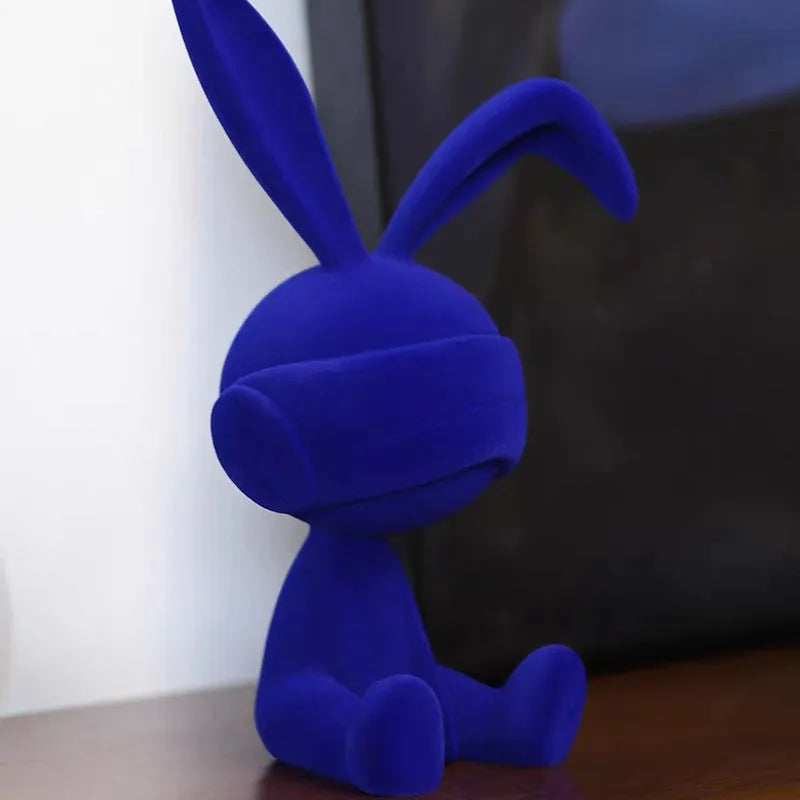 Green resin blindfold rabbit table ornament with suede details on a wooden shelf.