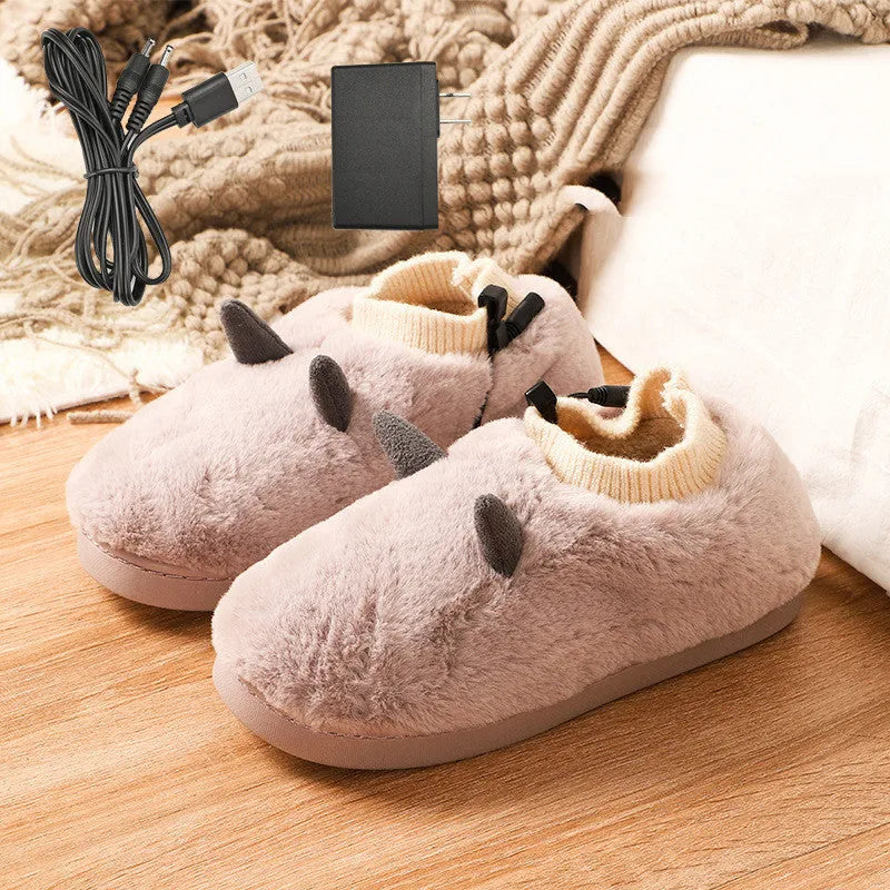 Black USB heated slippers with soft velvet upper and a connected USB cable on a desk.