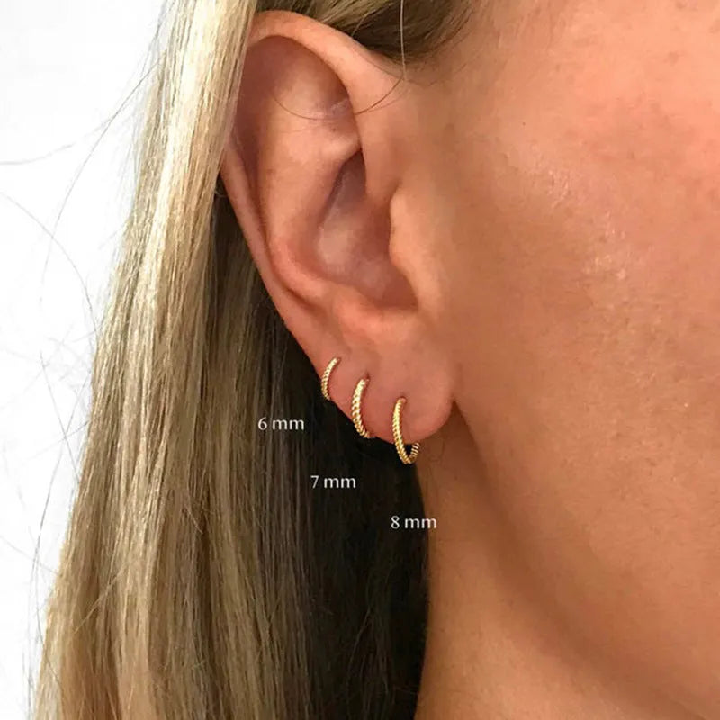 Close-up of twisted S925 sterling silver round ring earrings in gold colour on a plain background.