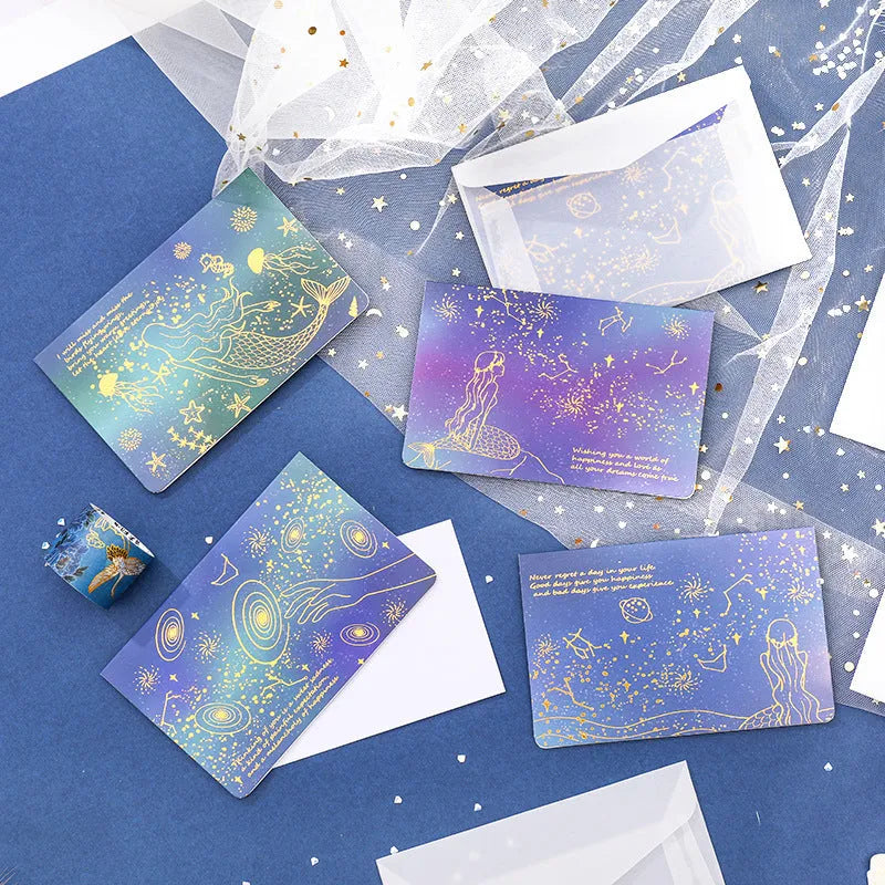Set of three gilded greeting card envelopes in galaxy colour designs on a dark background.