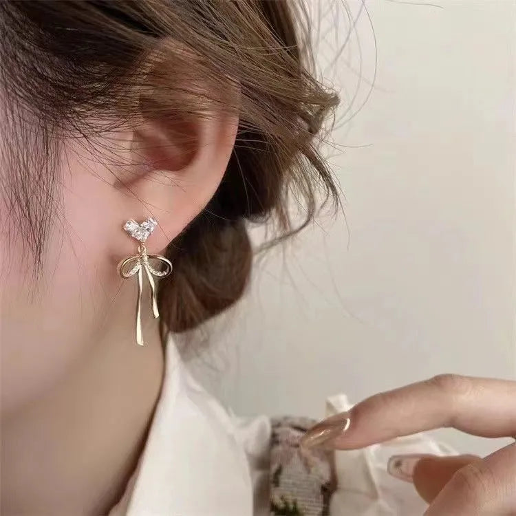 Pair of alloy bow tie ear studs with love heart zircon centre on light background