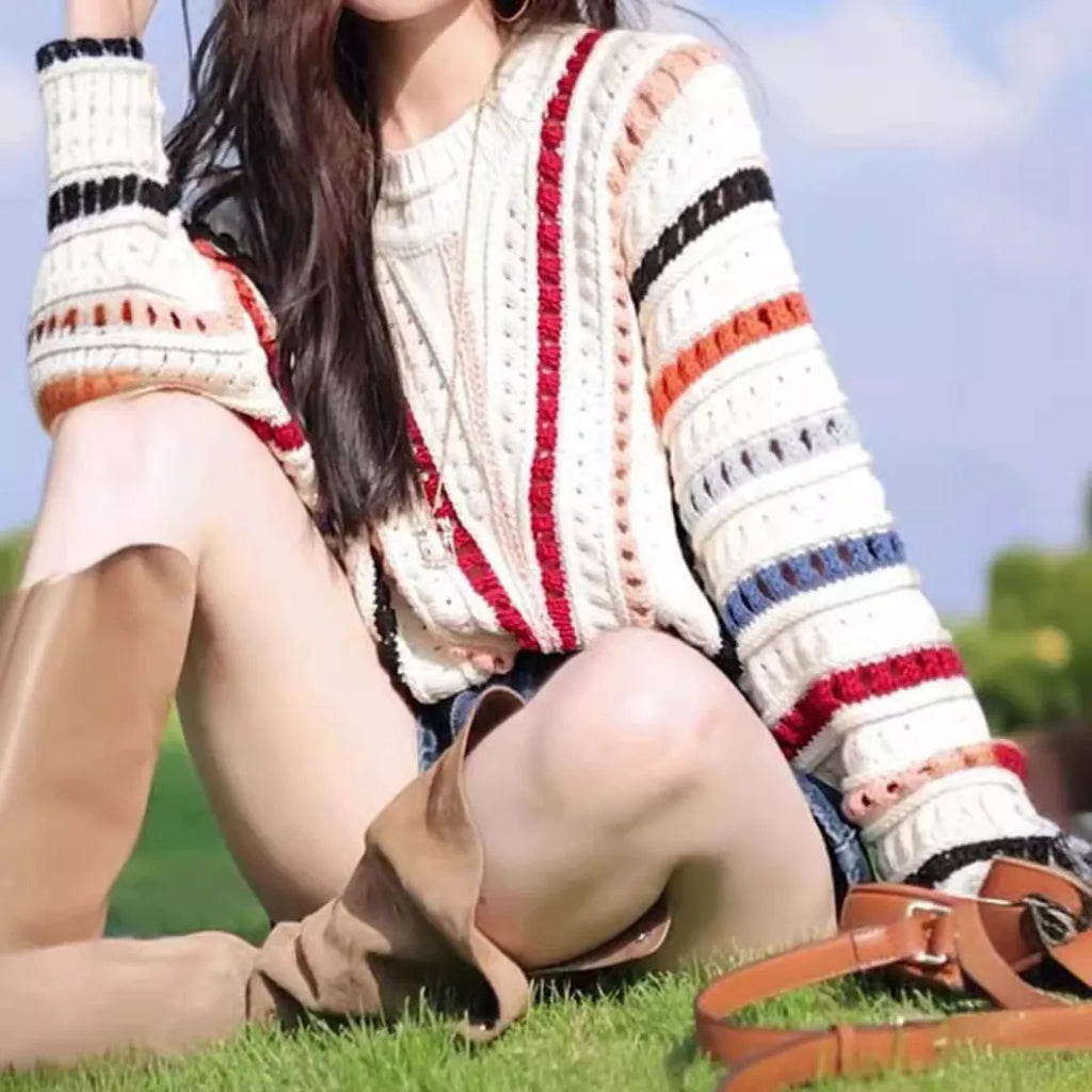 A woman's rainbow striped loose knit sweater with batwing sleeves on a hanger.