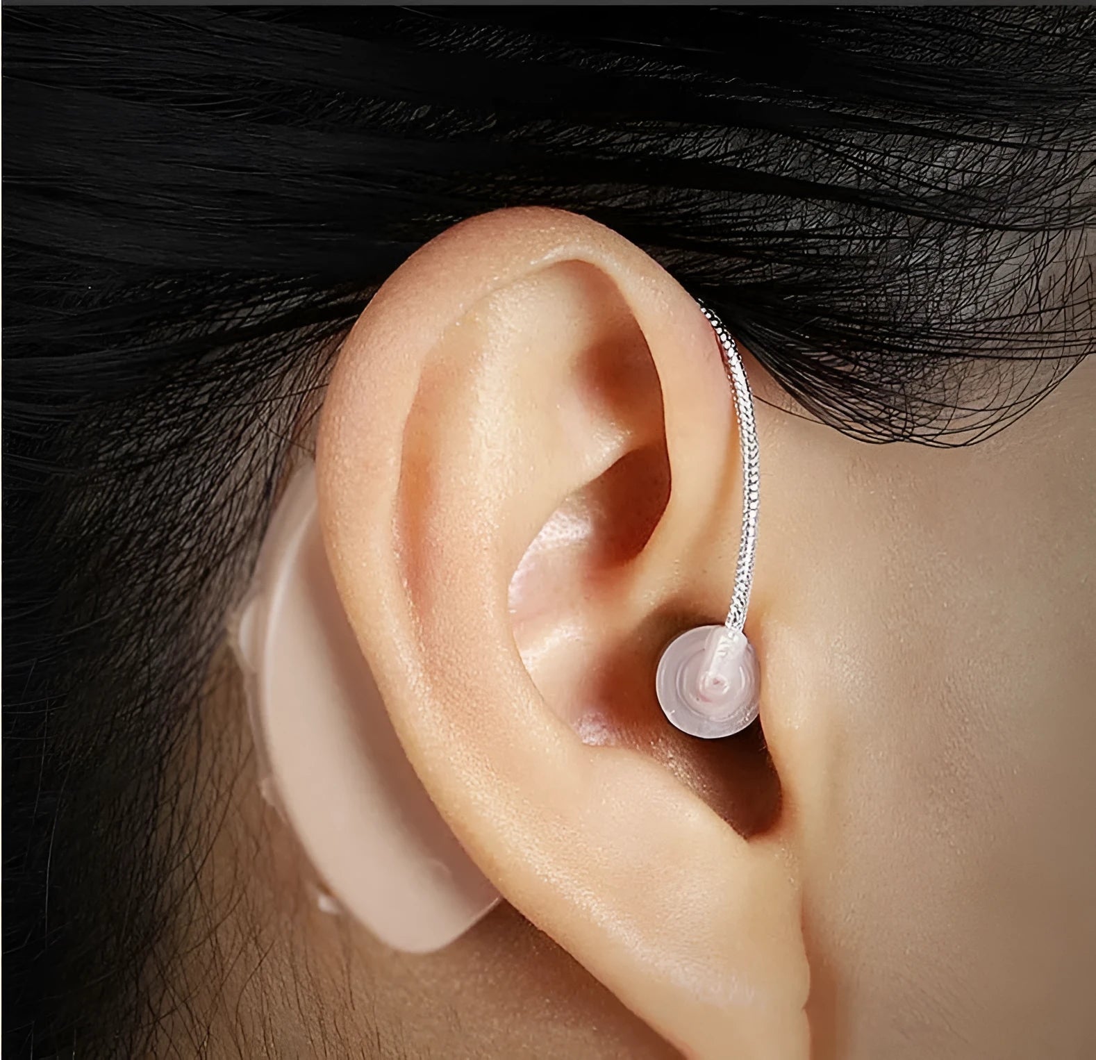 Black silicone rechargeable hearing aid amplifier with charging cable on a table.