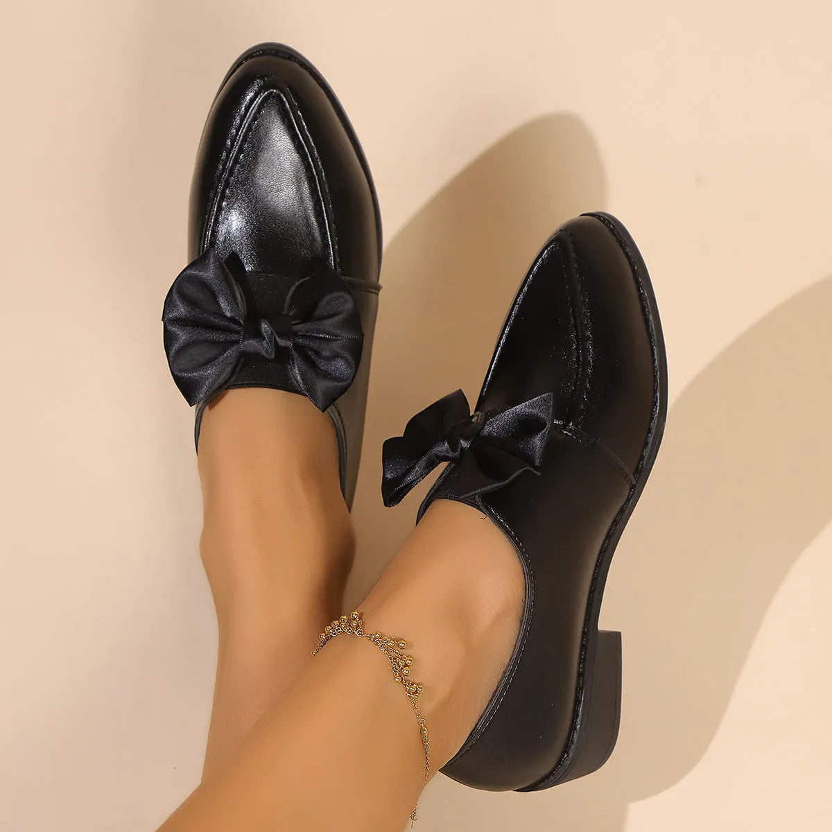 Women's black leather-look flat shoes with a decorative bow on the pointed toe.