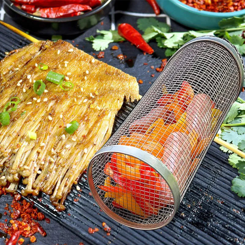 Round silver metal rolling barbecue basket with wire mesh and a hook, shown with vegetables inside on a grill.