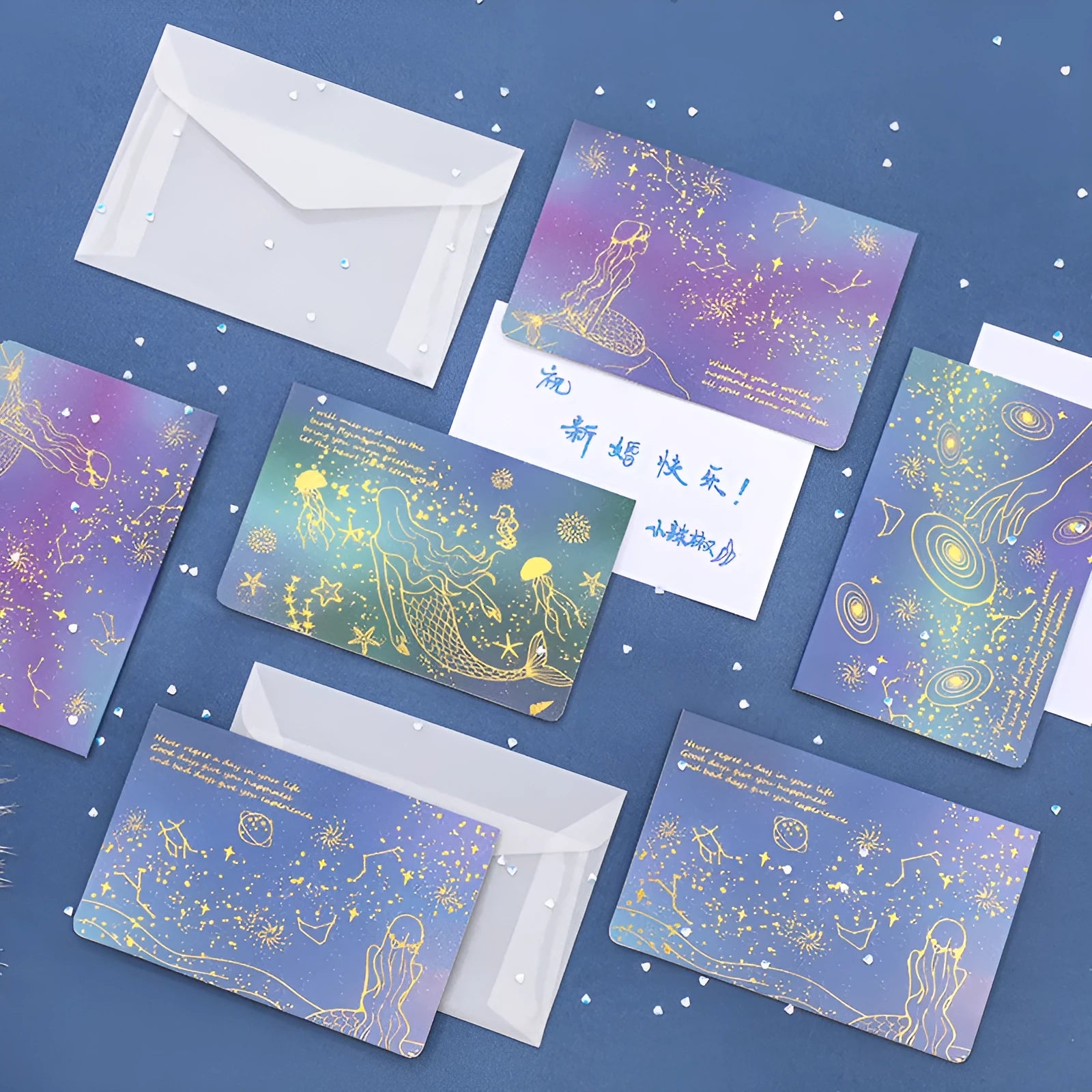 Set of three gilded greeting card envelopes in galaxy colour designs on a dark background.