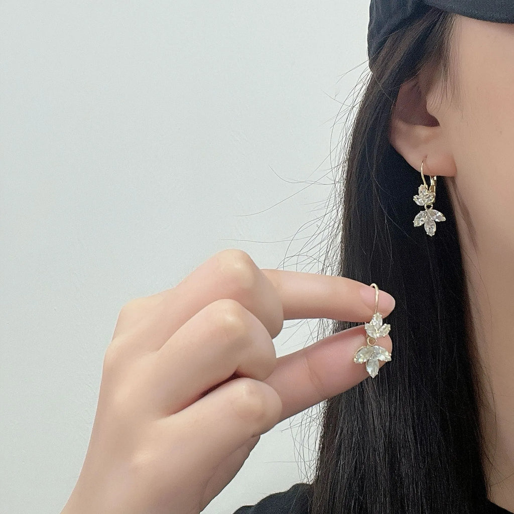 Platinum colour leaf-shaped earrings with inlaid zircon stones on white background