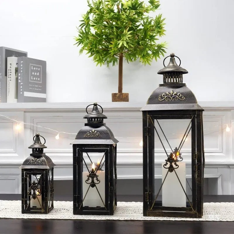 Black and white wrought iron floor standing storm lantern with tempered glass panels on a patio.