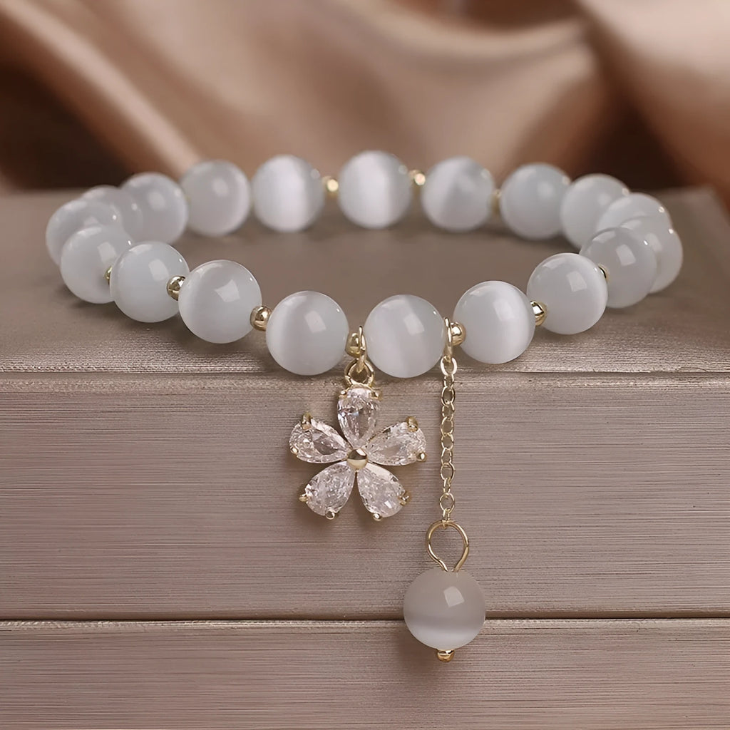 White cat's eye stone women's bracelet with flower and tassel charms on a morganite safety buckle.
