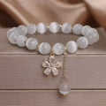 White cat's eye stone women's bracelet with flower and tassel charms on a morganite safety buckle.