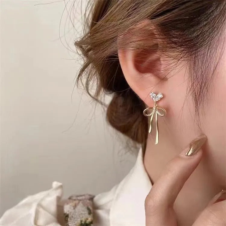 Pair of alloy bow tie ear studs with love heart zircon centre on light background